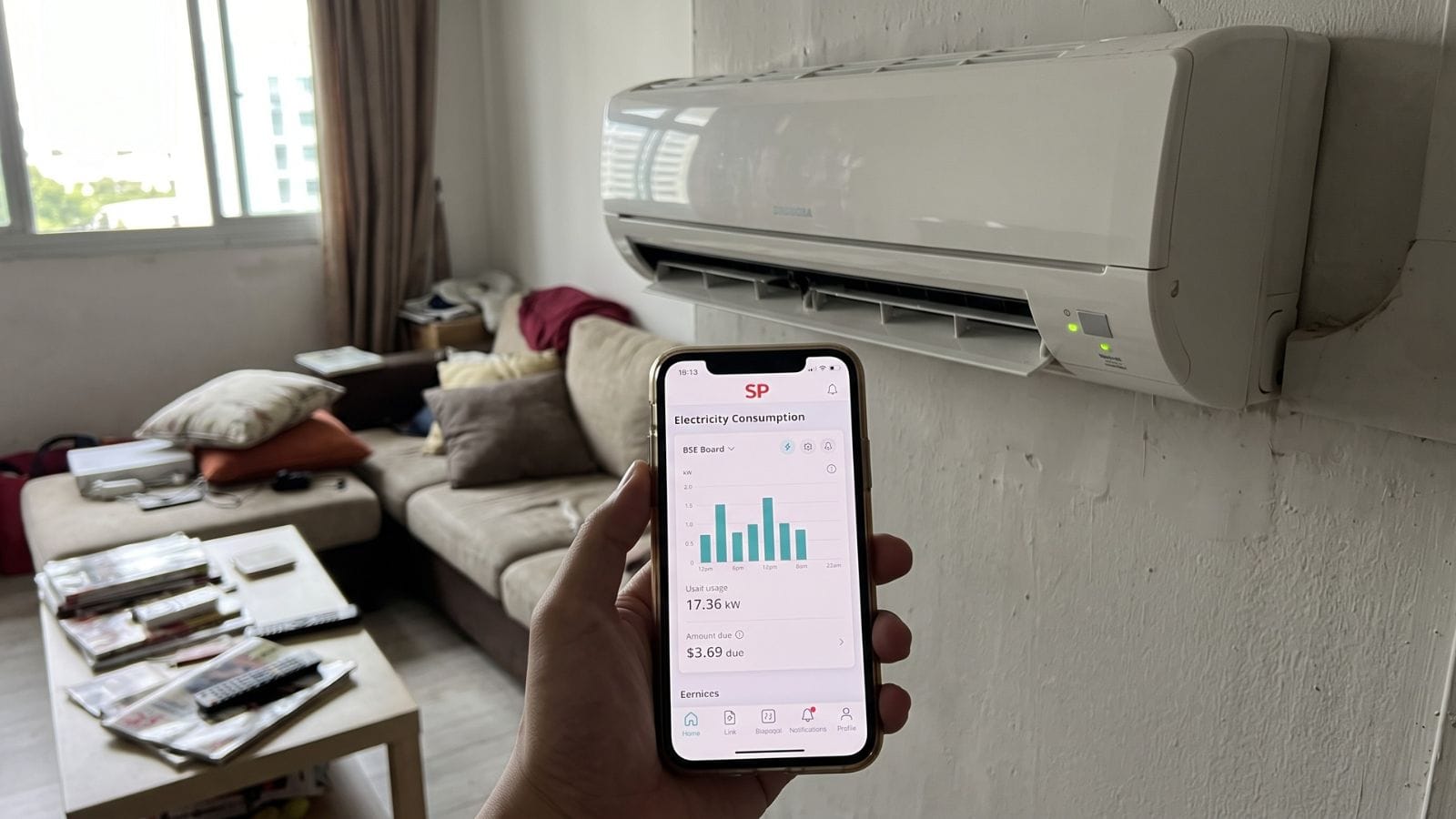 Singapore household electricity bill held up in front of a wall-mounted aircon unit in an HDB flat
