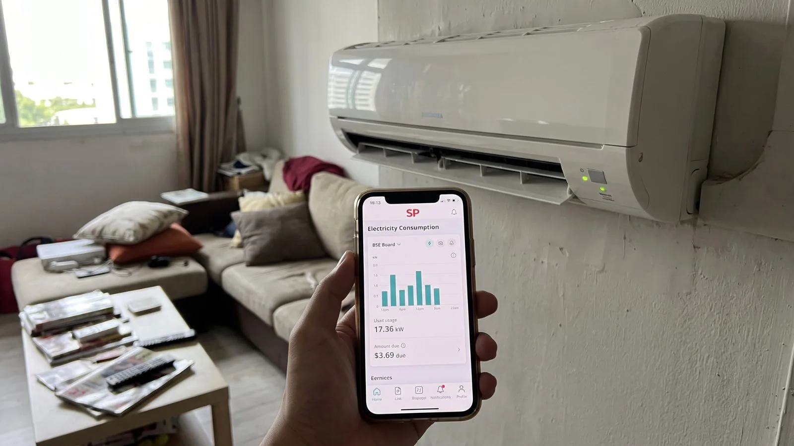 Singapore household electricity bill held up in front of a wall-mounted aircon unit in an HDB flat